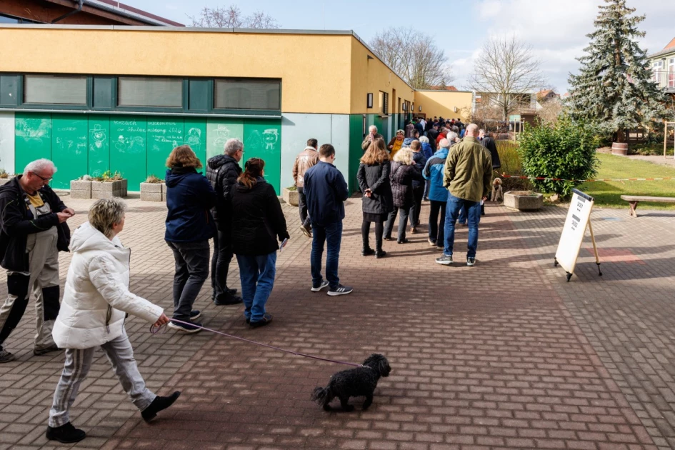 Voters walking toward a polling station in eastern Germany under a banner.