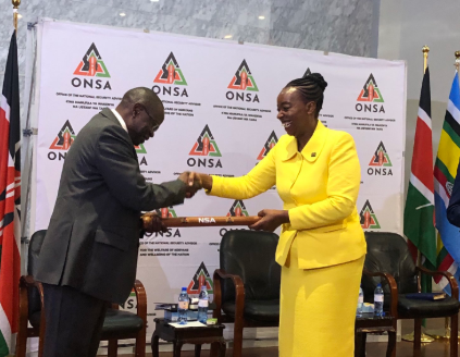 Monica Juma hands security baton to Joseph Boinett as she heads to Vienna